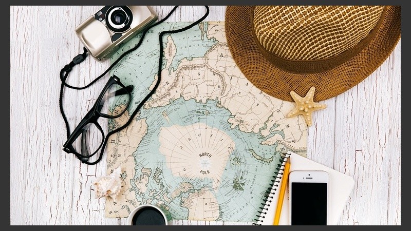 Smartphone lies on a notebook before a cup of coffee on the map, hat, camera and glasses around it