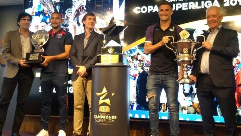 Luna y Pillud sostienen los trofeos que le posibilitaron a Tigre y Racing jugar esta final.